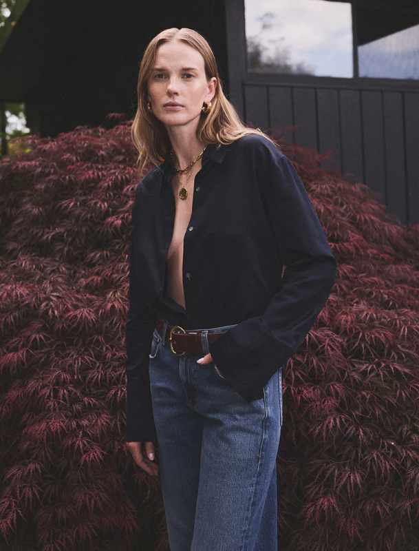 Woman wearing Camilla shirt from COH in navy and blue jeans standing in front of a dark building with red foliage | COH | MARKET